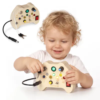 Imagen del producto de Panel de control "Mamabrum" con diseño de gamepad, que incluye 7 luces LED, interruptores y llaves, fabricado en madera contrachapada y metal. Dimensiones: 10 x 14 x 5,5 cm. Recomendado para niños a partir de 3 años