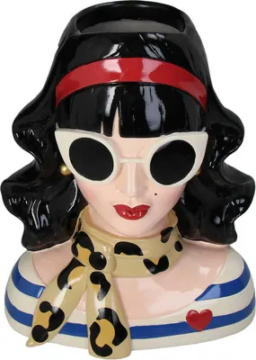A ceramic vase shaped like a woman's head, decorated with a red headband, white sunglasses, a leopard print scarf, and a striped top with a red heart.