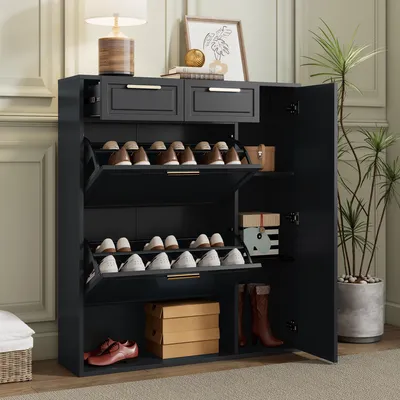 A dark gray shoe cabinet with two drawers and multiple shelves, filled with shoes and boxes, placed in a room with a plant and a lamp.