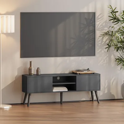 A dark gray TV stand with a TV mounted above it, in a living room setting with a plant and a lamp.