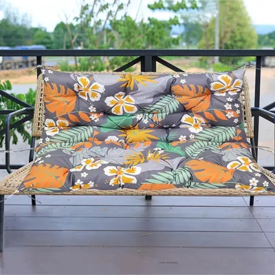 A cushion on a bench on a porch with trees and sky in the background.