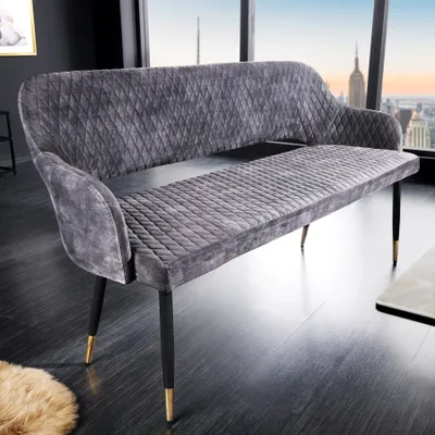 A gray velvet bench with diamond quilting sits in a modern room with large windows overlooking a city skyline.