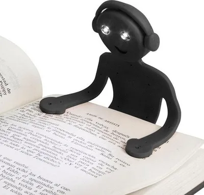 A black book light shaped like a person with headphones is clipped onto an open book.