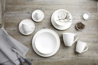 A flat lay of white ceramic tableware set on a wooden surface.