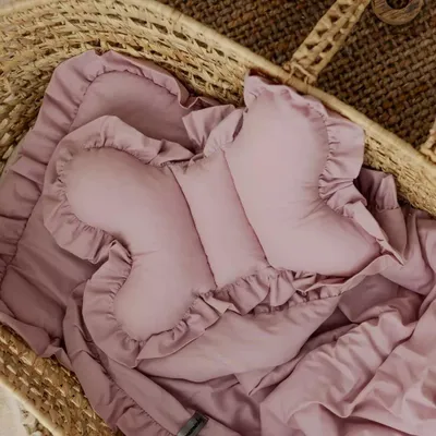 A pink butterfly-shaped baby pillow and blanket are placed inside a woven basket.