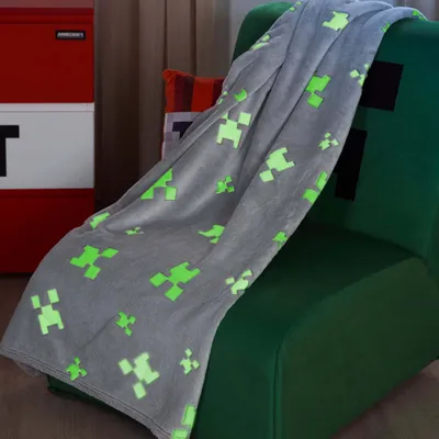 A Minecraft-themed blanket draped over a green chair, with a red and white TNT-like storage unit in the background.