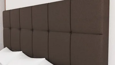A close-up view of a brown upholstered headboard with white pillows in the foreground.