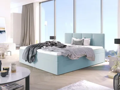 A light blue upholstered bed with bedding and pillows in a bright, modern bedroom with large windows.