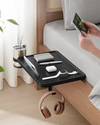 A bedside table attached to a bed, holding various items and being used by a person.