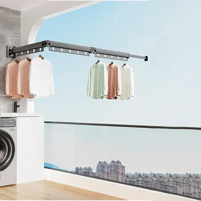 A balcony with a washing machine and a retractable clothes drying rack mounted on the wall, with clothes hanging on it. The background shows a cityscape under a blue sky.