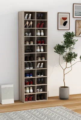 A tall, narrow shoe rack filled with shoes, placed against a white wall next to a potted plant.