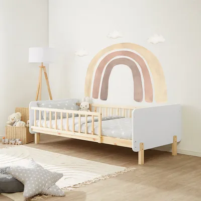 A child's bedroom with a bed, rainbow wall decal, and toys.