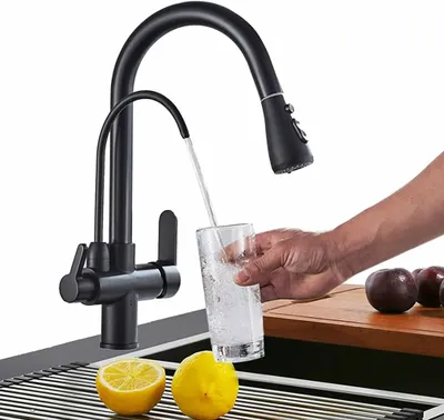 A black kitchen faucet dispensing water into a glass, with lemons and plums in the foreground.