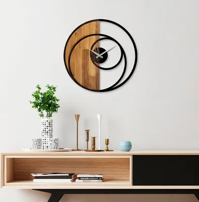 A modern wall clock with a wooden and metal design is displayed on a white wall above a wooden console table with decorative items.