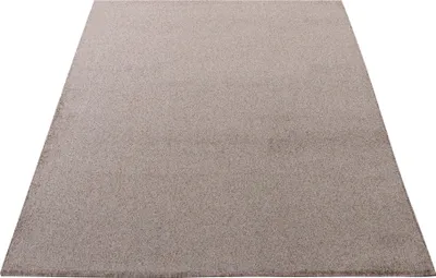A plain beige rug is shown from a slightly elevated angle against a white background.