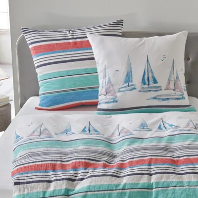 A close-up view of bedding with a nautical theme, featuring pillows and a duvet cover with sailboat and stripe patterns.