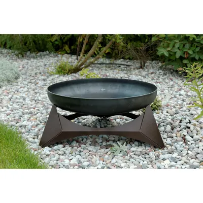 A fire pit with a copper-colored base sits on a bed of gravel in a garden setting.
