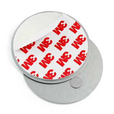 A close-up, overhead view of two round metal discs, one on top of the other, against a white background. The top disc has a peel-back adhesive backing with the 3M logo repeated multiple times in red and white. A small, circular magnet is visible on the bot