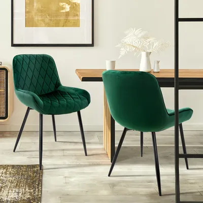 A dining room scene with two green velvet chairs at a wooden table.
