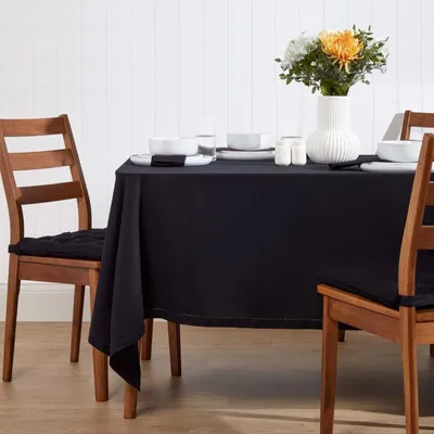 A dining table set with a black tablecloth, white dishes, and a vase of flowers.