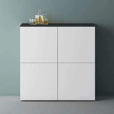 A modern cabinet with a dark top, featuring four white doors. On top of the cabinet are two glasses of amber liquid and a decanter filled with the same liquid.