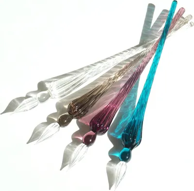 A collection of colorful glass dip pens arranged diagonally on a white background, casting shadows.