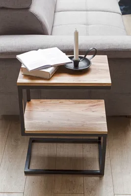 A side table with two shelves is placed next to a sofa, with a book and a candle on the top shelf.