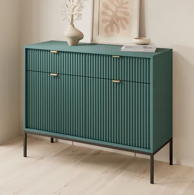 A teal dresser with gold handles sits on black legs in a room with light wood floors and a light-colored wall.