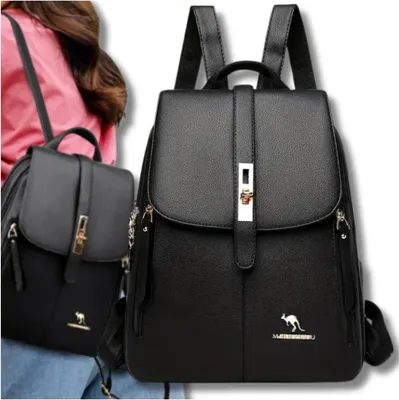 Two black leather backpacks are shown, one in the foreground and one slightly behind and to the left. A person's shoulder and arm are visible on the left side of the image, wearing a pink top.