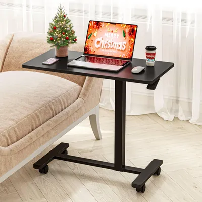 A black adjustable height table with a laptop, Christmas tree, and coffee cup on it, placed next to a beige sofa.