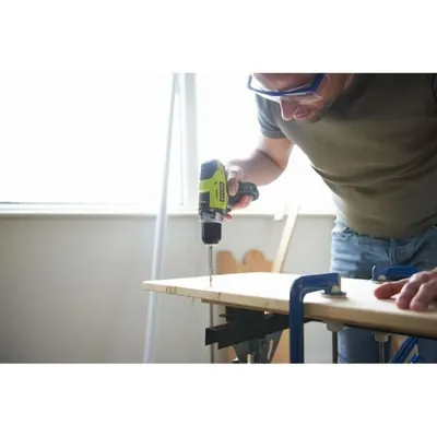 A man is using a cordless drill to drill into a piece of wood.