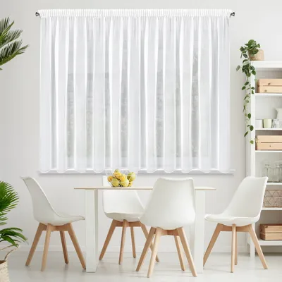 A white sheer curtain hangs over a window, with a dining table and chairs in the foreground.