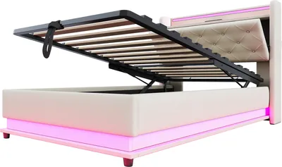 A beige upholstered bed frame with its storage compartment open, revealing wooden slats and a hydraulic lift mechanism. The bed has integrated pink LED lighting along its base and headboard.
