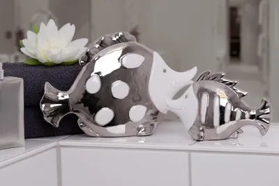 Two decorative fish figurines on a bathroom counter next to a folded towel and a white flower.