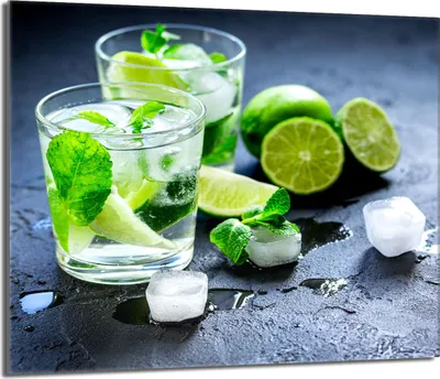 Two glasses of mojitos with limes and mint leaves on a dark surface.