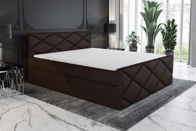 A luxurious bedroom setting with a brown upholstered boxspring bed as the main focus, placed on a rug in front of large windows with plants.