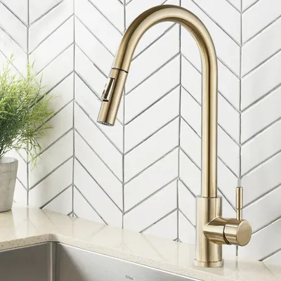 A gold kitchen faucet is shown in front of a white herringbone tile backsplash.