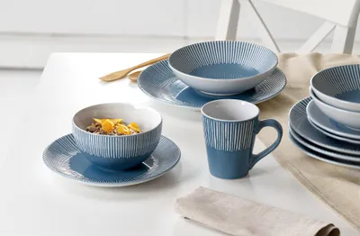 A set of blue and white striped ceramic dishes, including bowls, plates, and a mug, arranged on a white table.