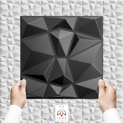 Hands holding a black 3D wall panel in front of a white textured wall.