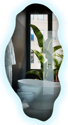 A modern bathroom with a freestanding bathtub and a large window overlooking a city building, with a large tropical plant in the foreground.