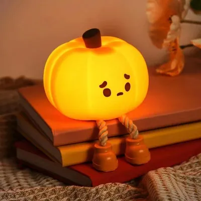 A cute, glowing pumpkin-shaped night light with a sad face sits on a stack of books.