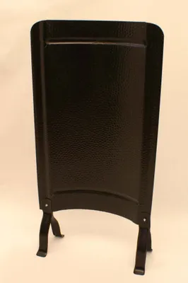 A black metal fire screen with a textured surface and curved base, standing on two legs.
