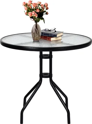 A round glass-top table with a black metal frame, decorated with a vase of pink flowers and two books with glasses on top.