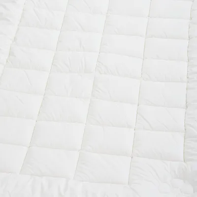 A close-up, overhead view of a white quilted blanket or comforter.