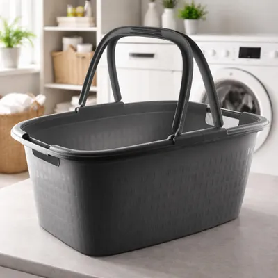 A dark gray laundry basket with handles sits on a countertop in front of a washing machine and shelves with laundry supplies.