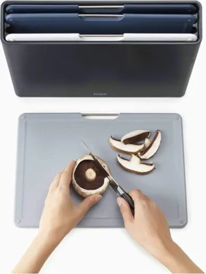 A set of cutting boards in a storage container is shown above a cutting board where someone is slicing a mushroom.