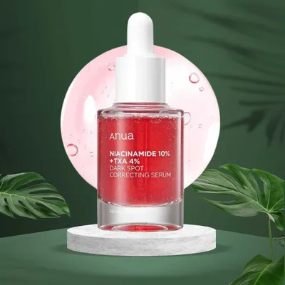 A bottle of serum is displayed on a pedestal with green foliage in the background.