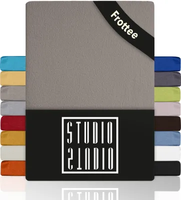 A product image displaying a taupe fitted sheet with a stack of other colored fitted sheets on the left and right sides. The product has a black band at the bottom with a white logo.