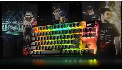 A gaming keyboard is displayed in front of a collage of esports imagery, including players and a trophy.