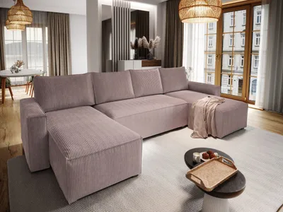 A modern living room with a large U-shaped sofa as the main focus, decorated with a throw blanket. A coffee table with decorative items is in front of the sofa, and a dining area is visible in the background.